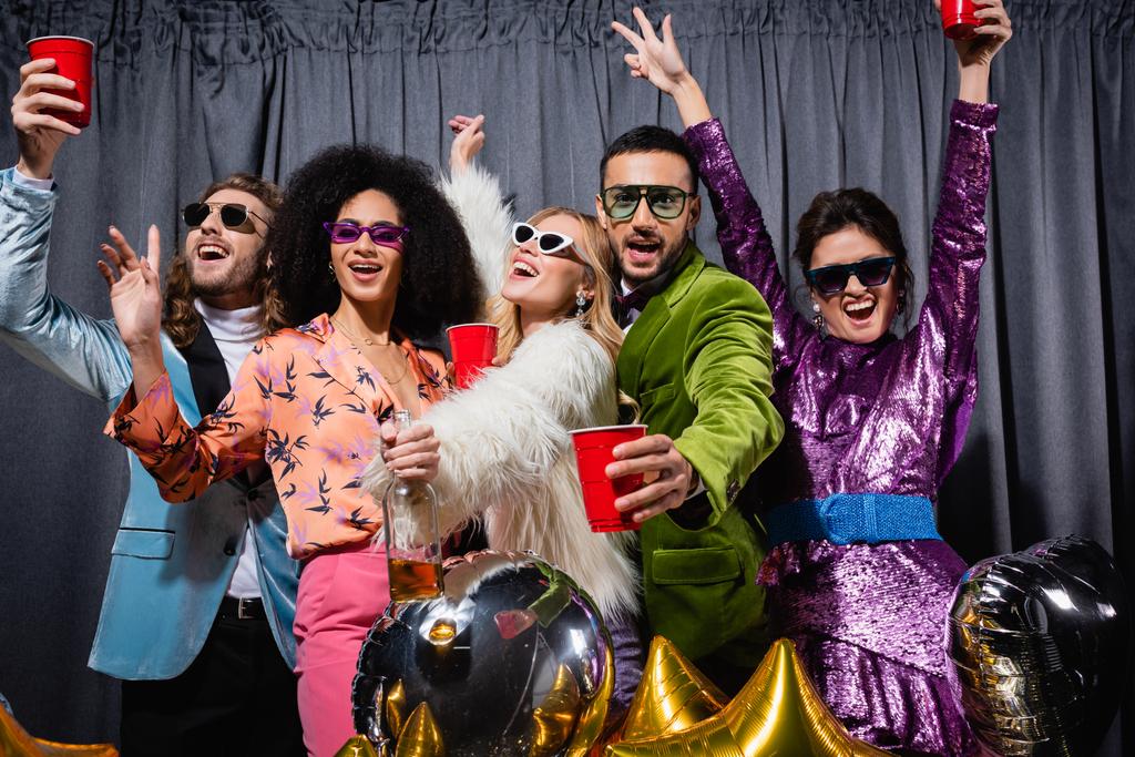 χαμογελαστοί διαφυλετικοί φίλοι με γυαλιά ηλίου που κάνουν πάρτι σε γκρι φόντο - Φωτογραφία, εικόνα