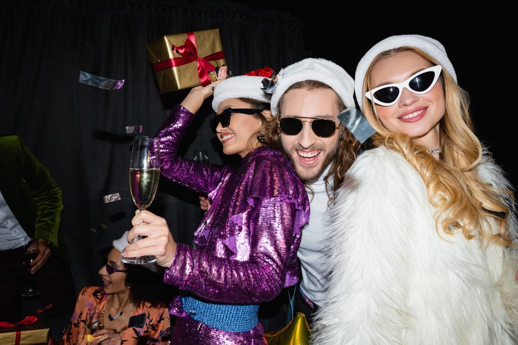 Счастливые друзья в санта-хатах пьют шампанское и встречают Новый год на сером фоне - Фото, изображение