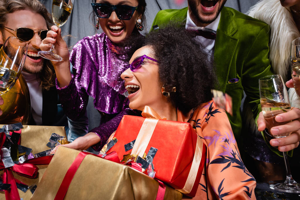 donna afroamericana sorridente con scatole regalo seduta tra amici interrazziali su sfondo grigio - Foto, immagini