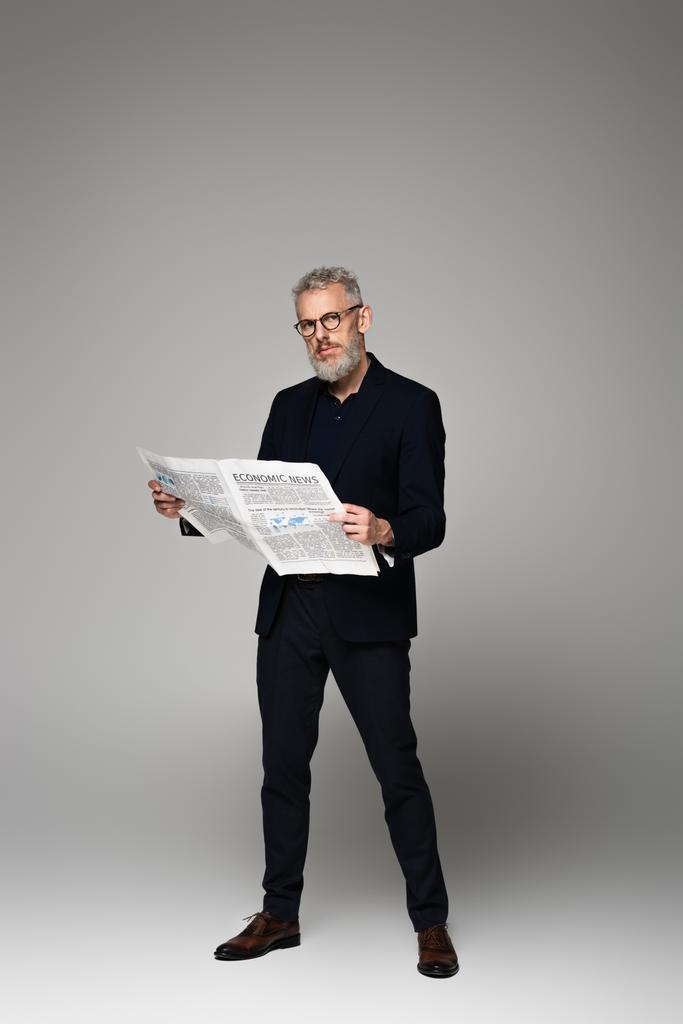 täysi pituus keski-ikäinen mies lasit ja puku tilalla taloudellinen sanomalehti harmaa - Valokuva, kuva