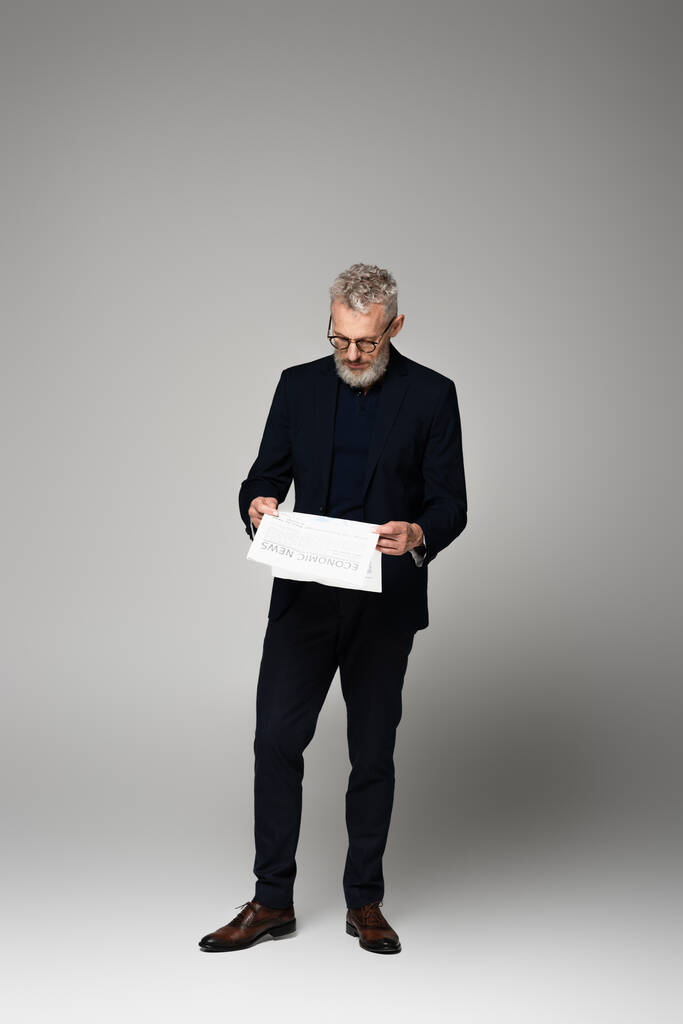 повна довжина середнього віку бізнесмен в окулярах читає газету на сірому
 - Фото, зображення