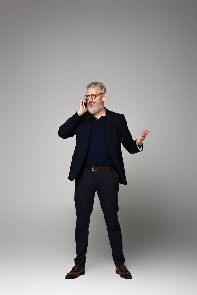 pełna długość szczęśliwy człowiek z siwymi włosami rozmawiając na smartfonie podczas gestykulacji na siwy - Zdjęcie, obraz