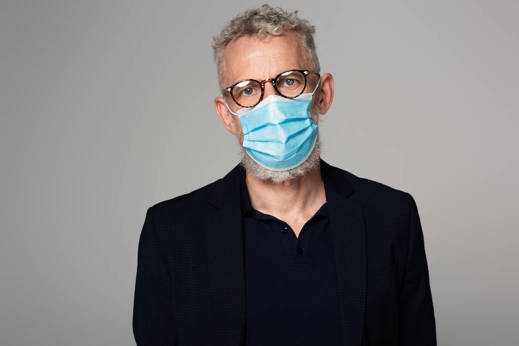 muž středního věku s šedými vlasy v brýlích a lékařské masky izolované na šedé  - Fotografie, Obrázek