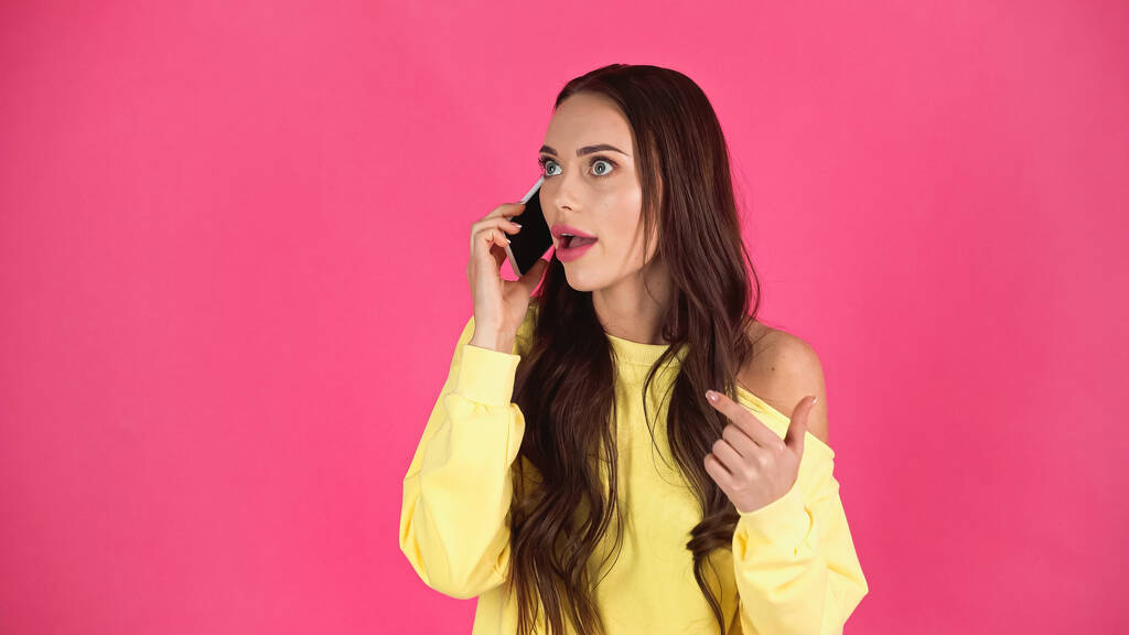 astonished young adult woman with open mouth speaking on cellphone isolated on pink   - Foto, imagen