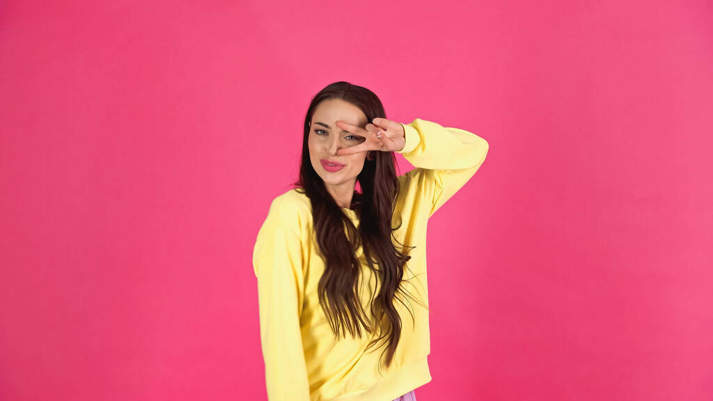 playful young adult woman with peace gesture near face isolated on pink - Fotografie, Obrázek