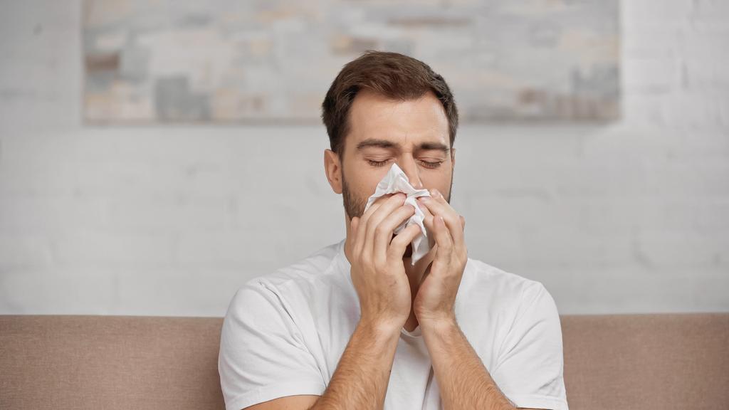 man with pollen allergy sneezing in napkin at home - Foto, imagen