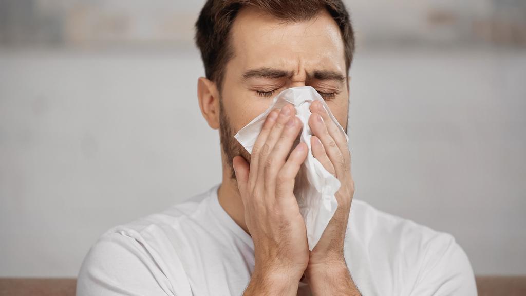 man with allergy sneezing in napkin at home - Foto, imagen