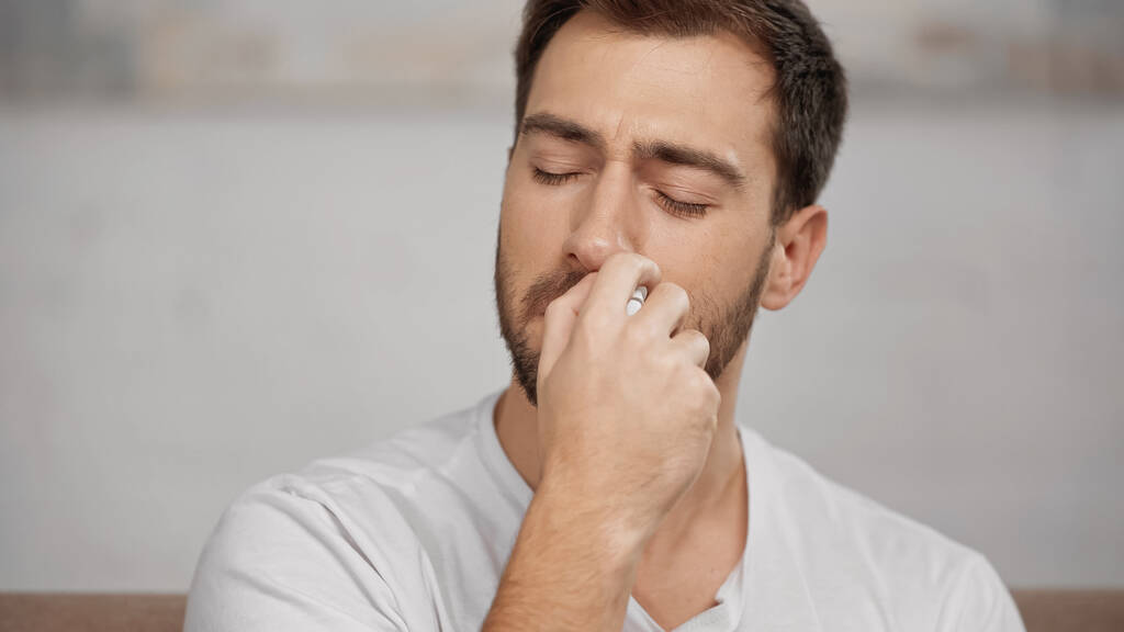 allergic man in white t-shirt using nasal spray at home  - Foto, immagini