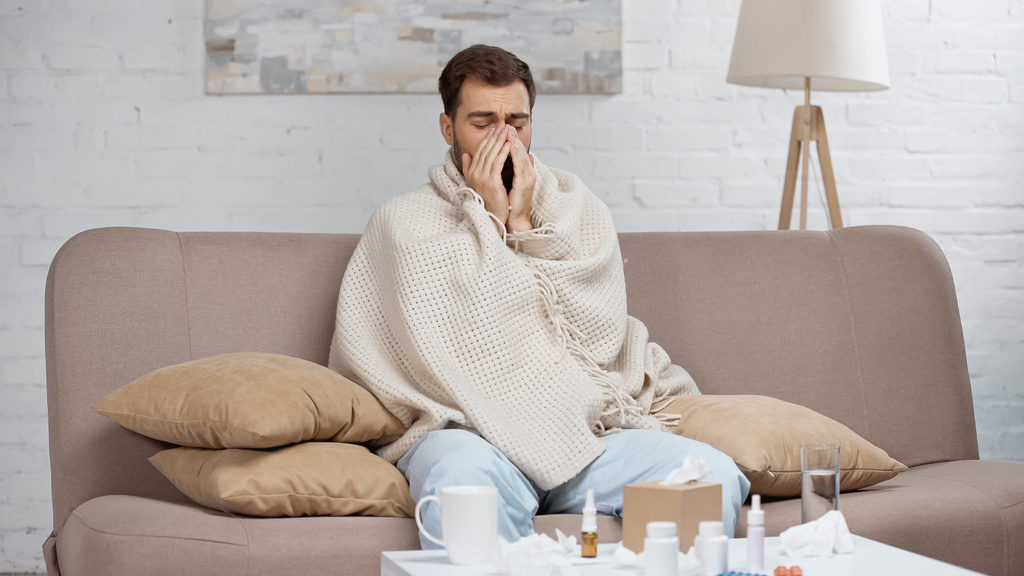 sick man sneezing near coffee table with drinks and bottles  - Foto, afbeelding