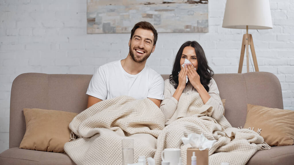 bearded man smiling near sick girlfriend sneezing in tissue  - Fotó, kép