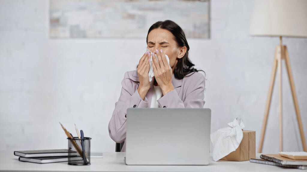 allergic businesswoman sneezing in tissue near laptop on desk - Photo, image