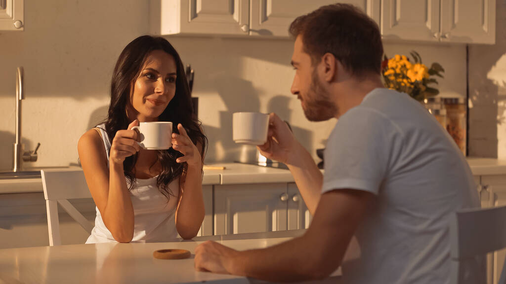 young woman holding cup of coffee and smiling near blurred boyfriend  - Photo, image