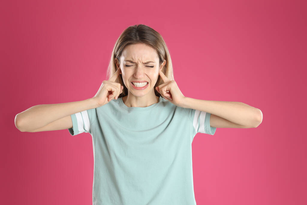 Емоційна молода жінка прикриває вуха пальцями на рожевому фоні
 - Фото, зображення