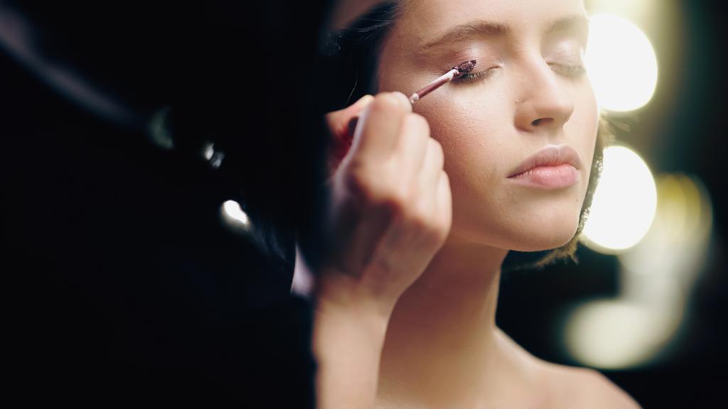 maquillador borroso aplicando sombra de ojos líquida en el párpado del modelo  - Foto, imagen