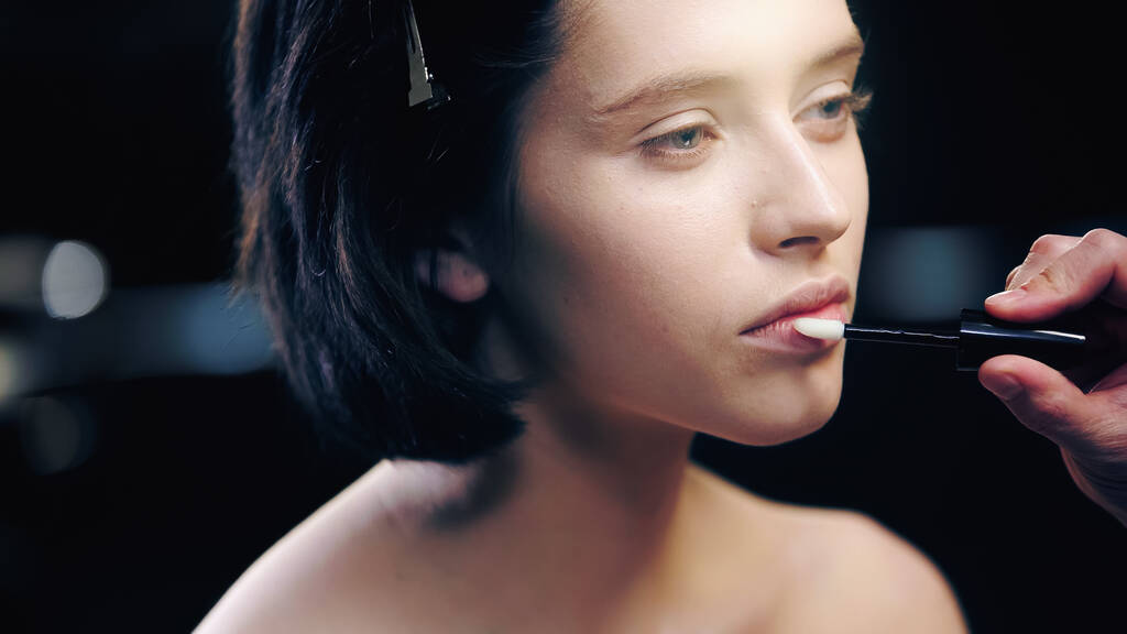 makeup artist εφαρμογή lip gloss στα χείλη του μοντέλου με γυμνούς ώμους  - Φωτογραφία, εικόνα