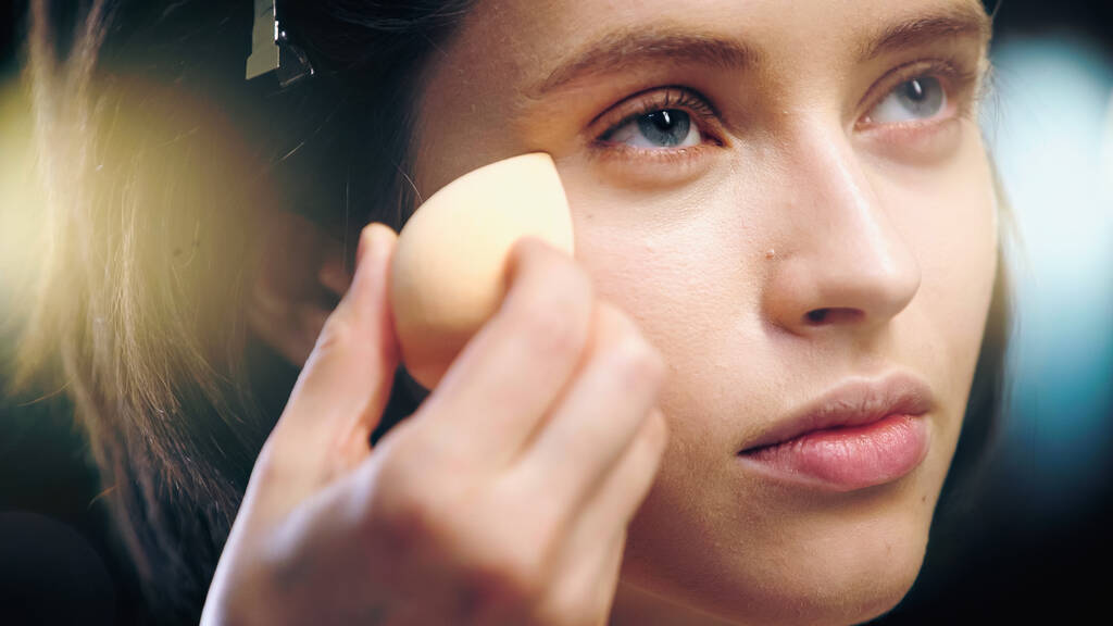 blurred makeup artist applying makeup foundation with cosmetic sponge on face of model - Photo, Image
