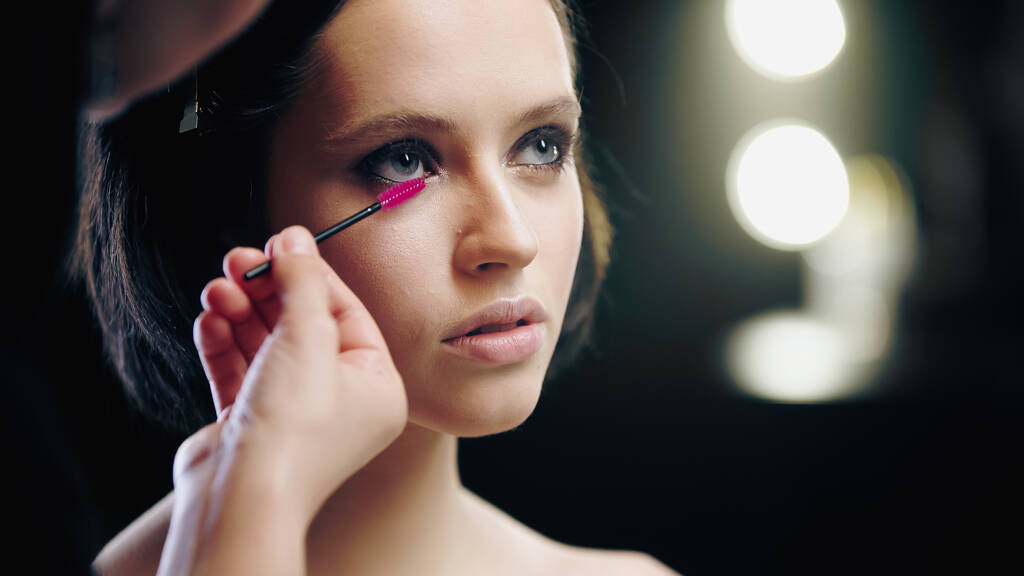 makeup artist applying mascara on eyelashes isolated on black - Photo, Image