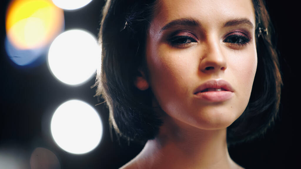 mladá žena s make-up při pohledu na kameru se zadním světlem na rozmazaném pozadí - Fotografie, Obrázek
