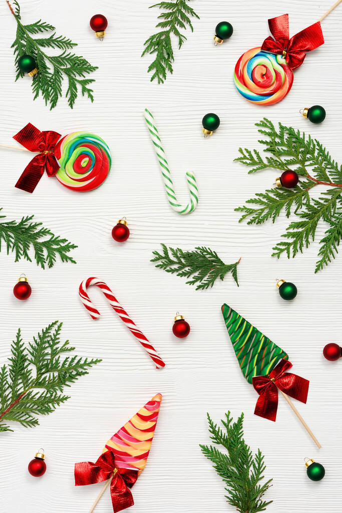 Kerstcompositie. Kerst snoep en snoep stokken, thuja takken, en Nieuwjaar kleine rode en groene ballen op witte houten tafel, bovenaanzicht, platte lay. - Foto, afbeelding