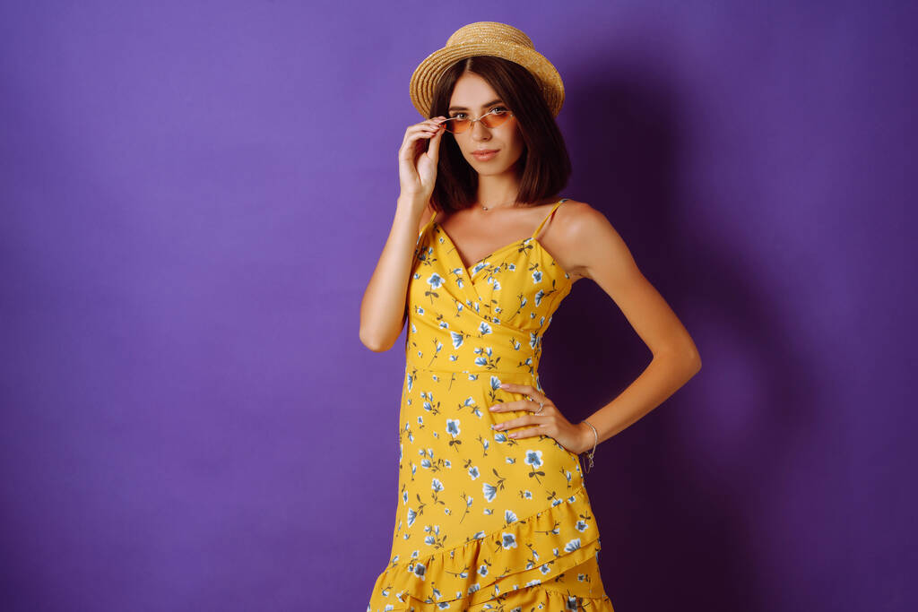 Mosolygó nő sárga ruhában és kalap pózol lila háttér. Divat, stílus, nyári koncepció.  - Fotó, kép
