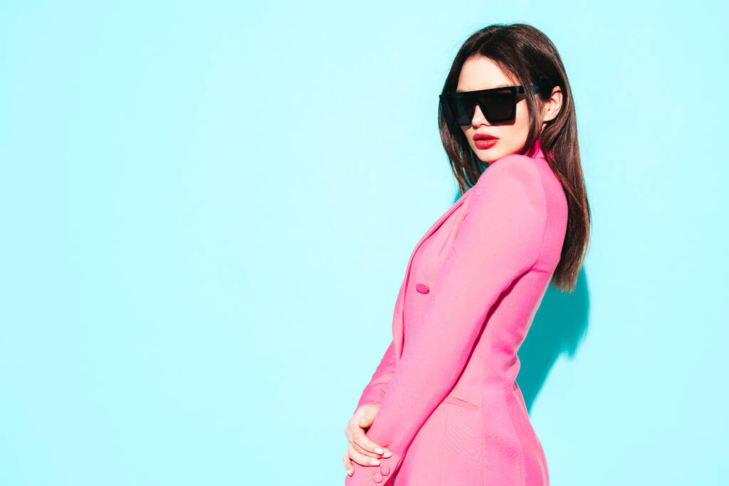 Retrato de alta moda de una joven hermosa morena que usa un bonito traje de verano rosado. modelo de moda exy posando cerca de la pared azul en studio.Fashion hembra en gafas de sol - Foto, Imagen