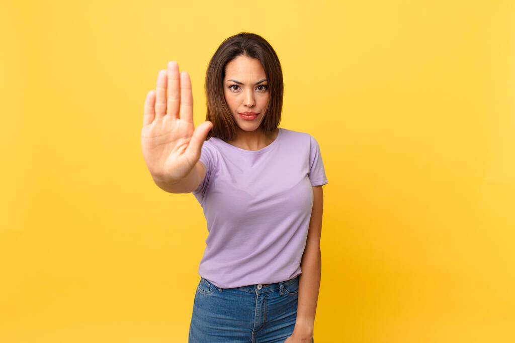 junge hispanische Frau sieht ernst und zeigt offene Handfläche, die Stopp-Geste macht - Foto, Bild
