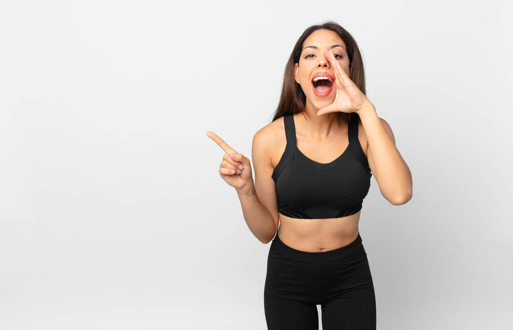 jonge Spaanse vrouw voelt zich gelukkig, geeft een groot geschreeuw met handen naast de mond. fitness concept - Foto, afbeelding