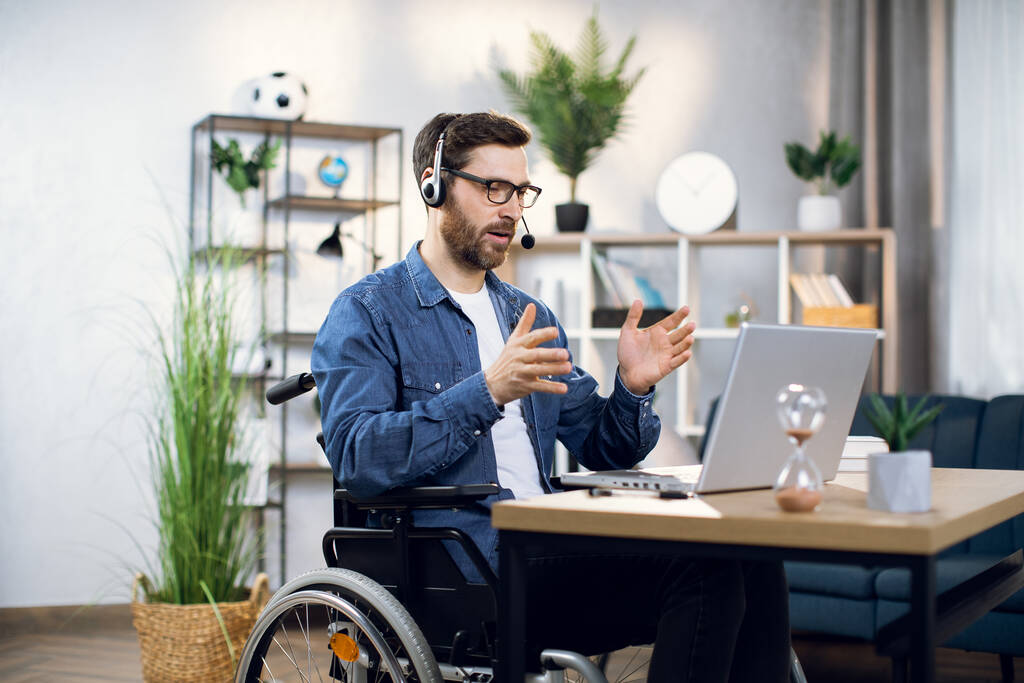 Hombre en silla de ruedas con auriculares y portátil para videollamada - Foto, Imagen