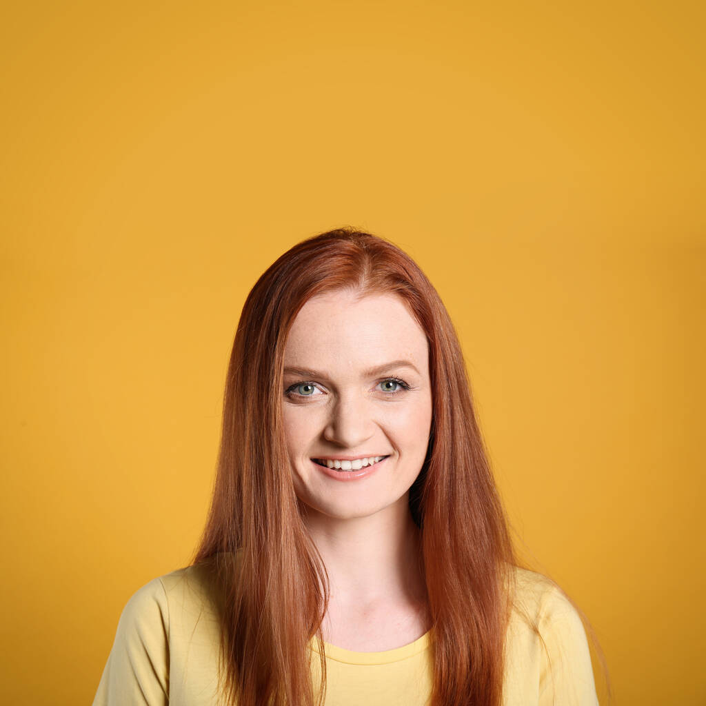 Çekici gülüşü ve sarı arka planda muhteşem kızıl saçları olan mutlu genç bir kadının samimi portresi. - Fotoğraf, Görsel