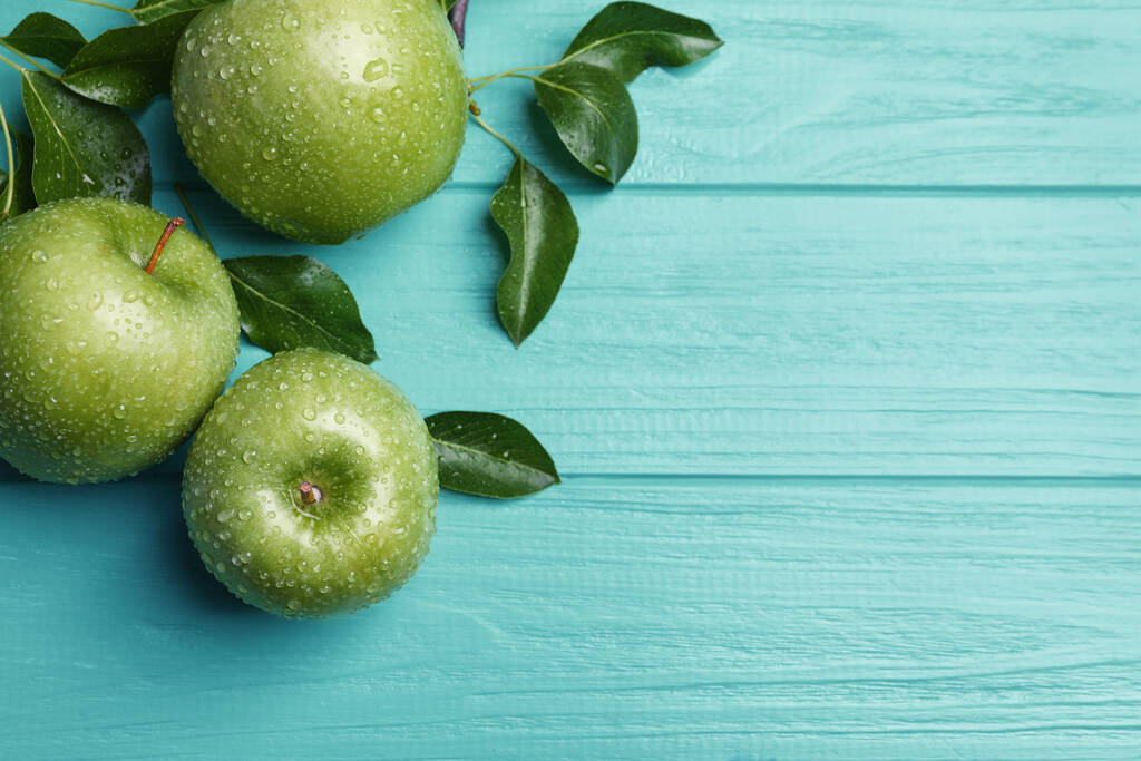 Свежие спелые зеленые яблоки с капельками воды на бирюзовом деревянном столе, плоский уголок. Пространство для текста - Фото, изображение