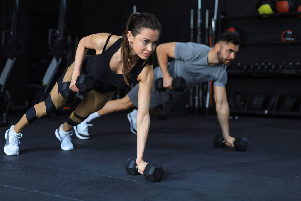 Starker Mann und starke Frau mit Hanteln in Plankenstellung im Fitnessstudio - Foto, Bild