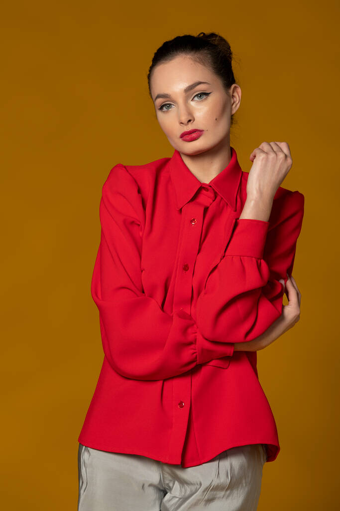 hermosa chica en camisa roja posando sobre fondo amarillo, vestido elegante y aspecto atractivo y maquillaje - Foto, imagen