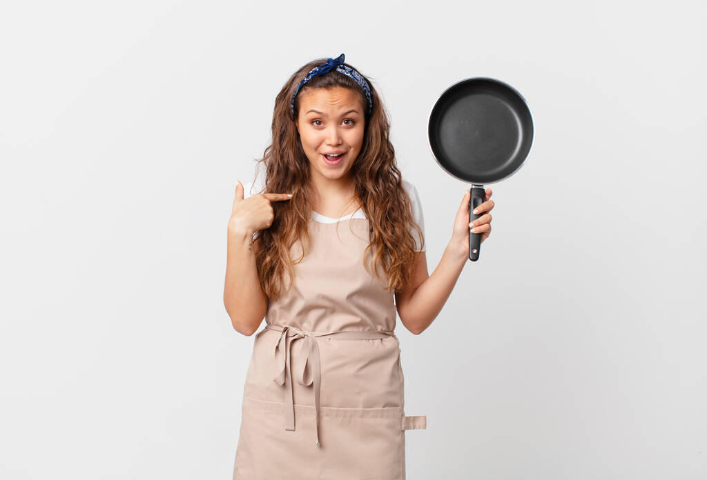fiatal csinos nő érzés boldog és rámutatva magára egy izgatott szakács koncepció és a kezében egy serpenyő - Fotó, kép