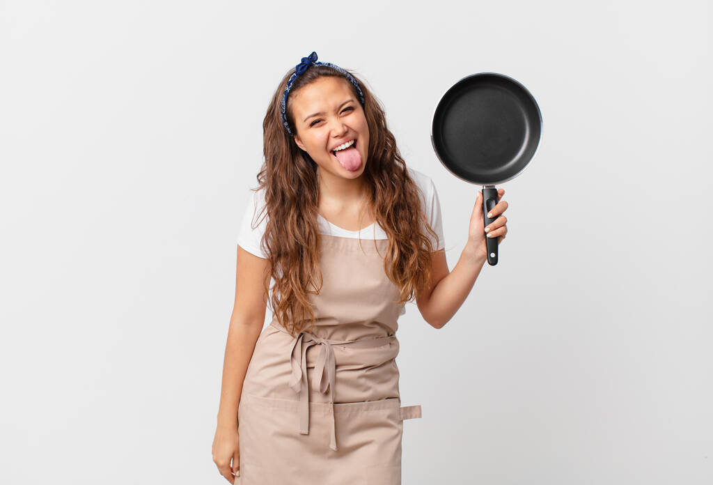 młoda ładna kobieta z wesołym i buntowniczym nastawieniem, żarty i wystające język z koncepcji szefa kuchni i trzymając patelni - Zdjęcie, obraz