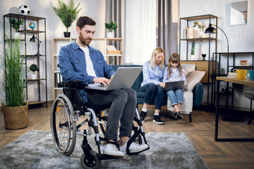 Uomo disabile e la sua famiglia utilizzando computer portatili a casa - Foto, immagini