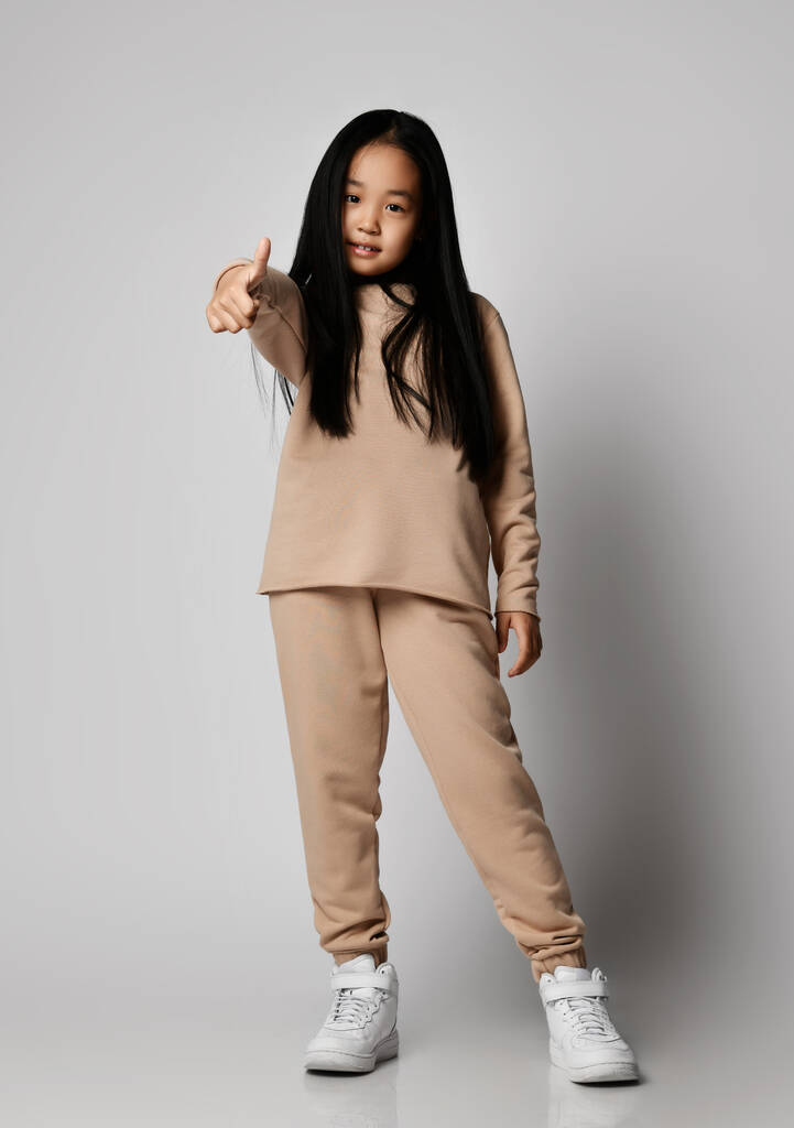 積極的なアジアの子供の女の子で緑のカジュアルスポーツウェア綿のパンツ,パーカー,ジャージーとスニーカースタンドジェスチャー親指アップ - 写真・画像
