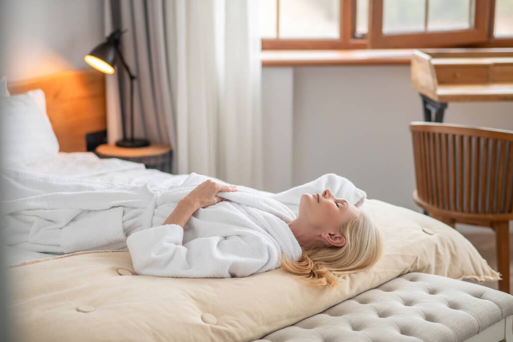 Una bella donna con un accappatoio bianco sdraiata su un letto - Foto, immagini