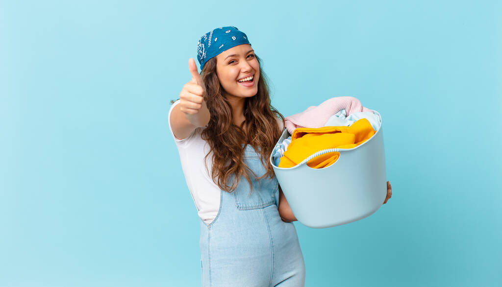 若い女性は誇りを感じ親指で積極的に微笑み洗濯籠を持っています - 写真・画像