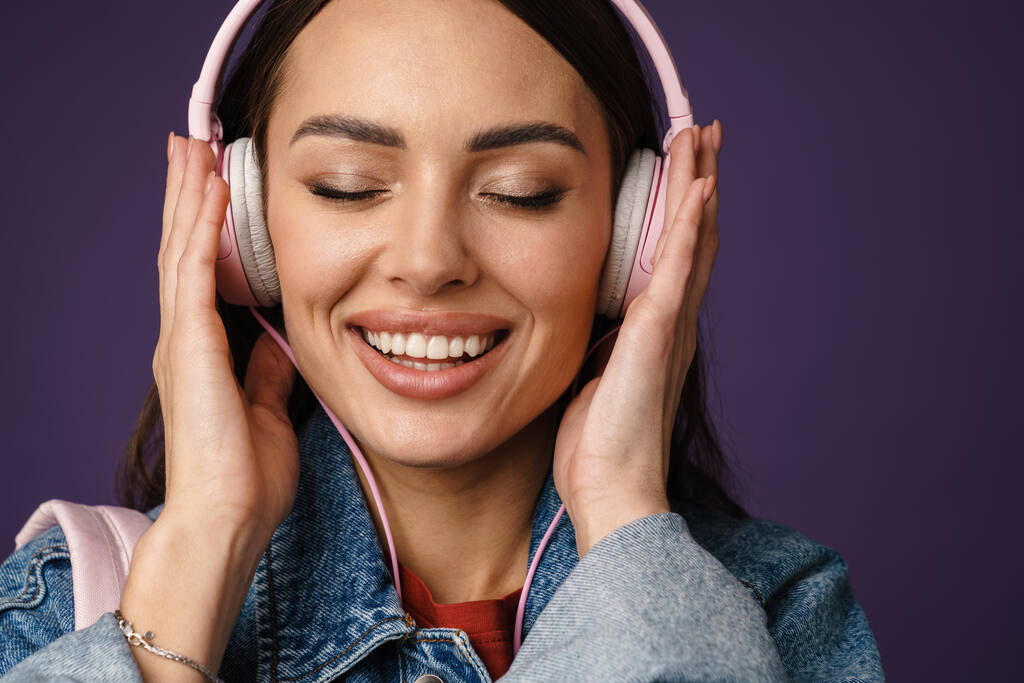 Alegre joven atractiva escuchando música con auriculares aislados sobre fondo violeta, de cerca - Foto, imagen