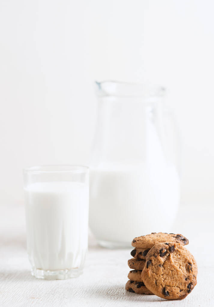 チョコレートチップクッキーとミルクを瓶と白い木の背景のガラスに入れ - 写真・画像