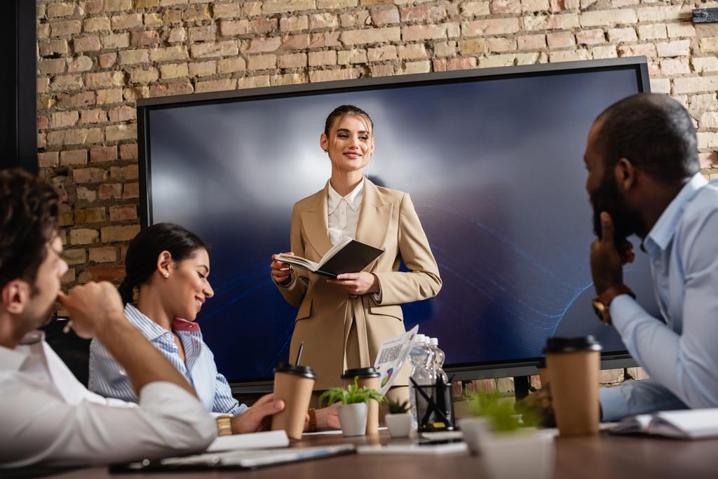 jeune femme d'affaires avec ordinateur portable debout près des partenaires d'affaires interracial dans la salle de conférence - Photo, image