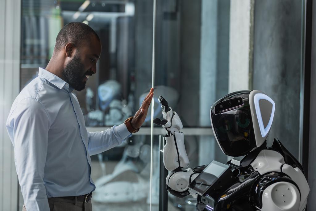 glücklich afrikanisch-amerikanischer Geschäftsmann gibt High Five an Roboter im Büro - Foto, Bild