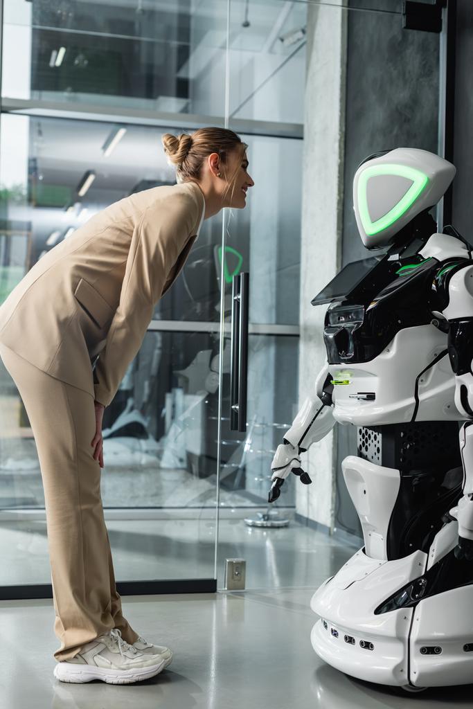 Genç iş kadınının ofisteki insansı robota uzun uzun bakışıyla. - Fotoğraf, Görsel