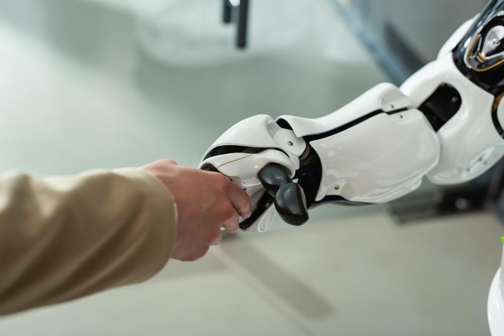 Teilansicht von Geschäftsfrau beim Händeschütteln mit Roboter im Büro - Foto, Bild