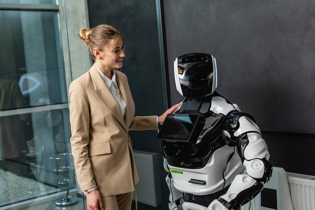 joyeuse femme d'affaires debout près du robot dans le bureau - Photo, image