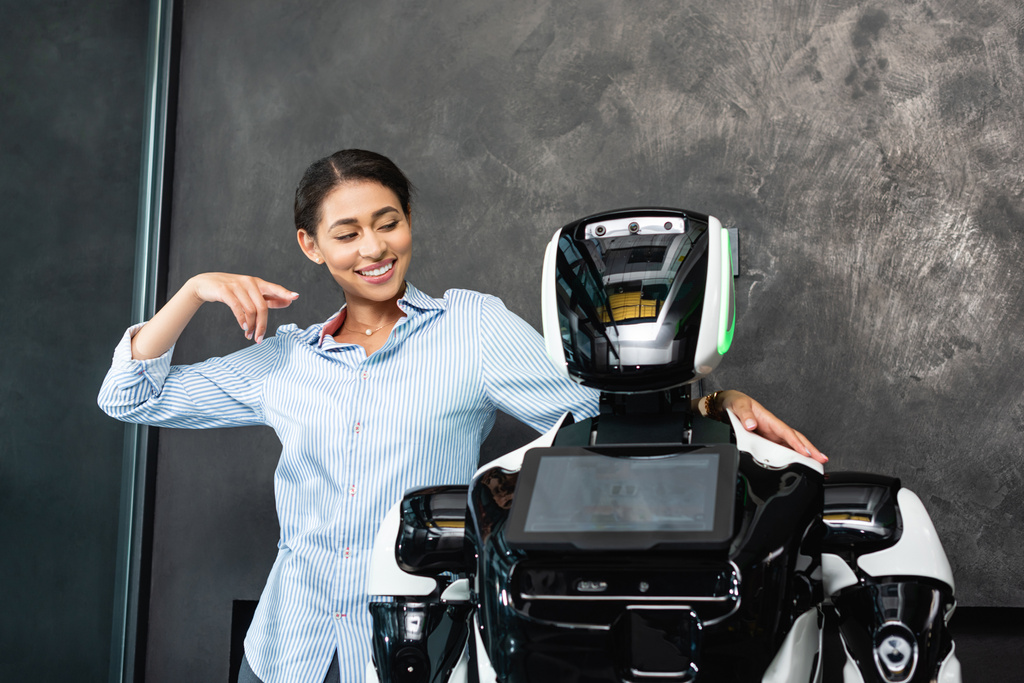 joyful african american businesswoman pointing at humanoid robot in office - Photo, Image