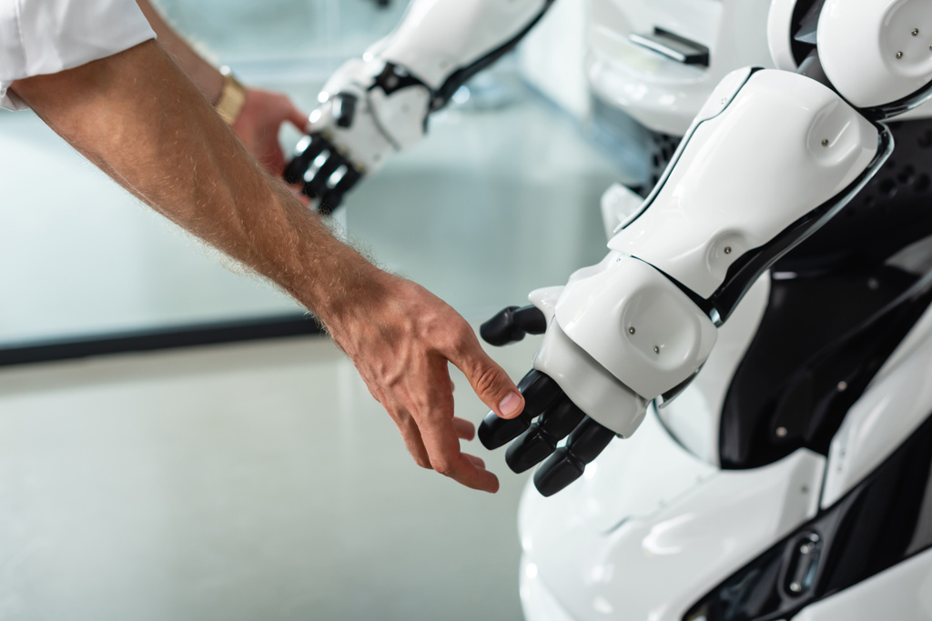 visão parcial do engenheiro tocando as mãos do robô humanoide no escritório - Foto, Imagem