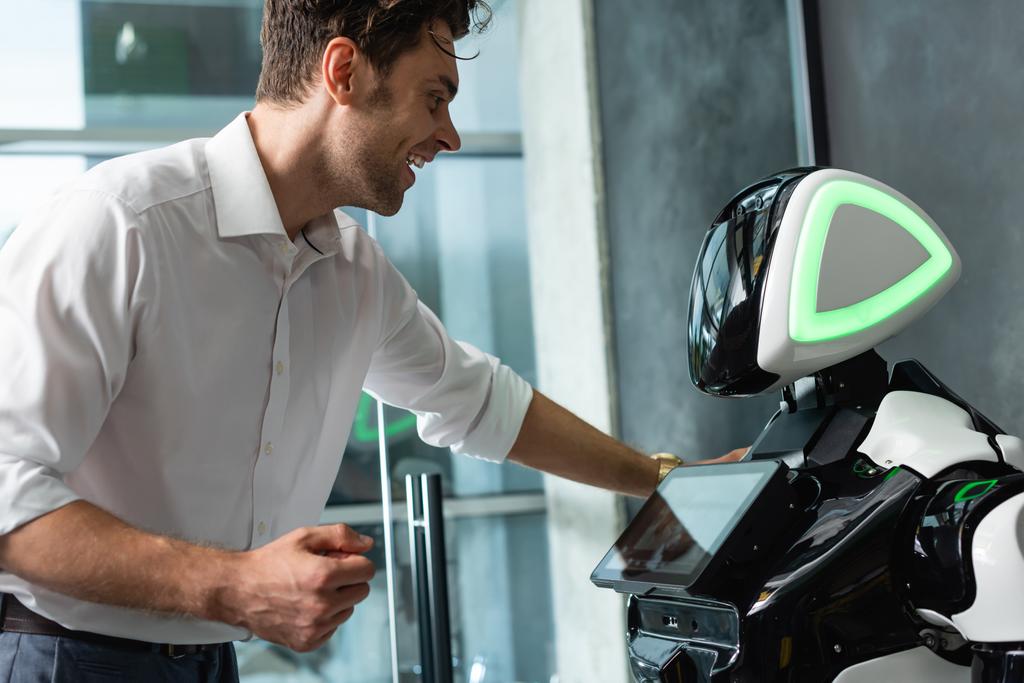 χαρούμενος επιχειρηματίας στέκεται κοντά ρομπότ στο γραφείο - Φωτογραφία, εικόνα