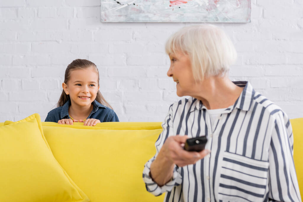 Enfant souriant à la grand-mère avec télécommande au premier plan flou  - Photo, image