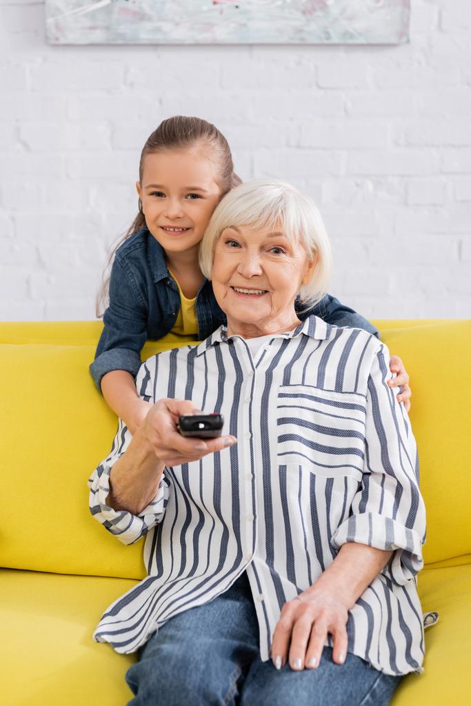 Gülümseyen çocuk evde televizyon izlerken büyükannesine sarılıyor.  - Fotoğraf, Görsel